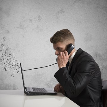 man in suit speaking on the phone in front of laptop small business phone systems